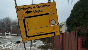 na zdjęciu żółta tablica informacyjna z napisem: zamknięt ul. Geodetów. Objazd